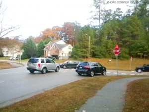 The three stop signs on the intersection of Pride Way and Oneal are marked with orange flags. The black Nissan (center) would have been able to easily turn right, but now must come to a complete stop at the stop sign, which leads to more congested traffic. 