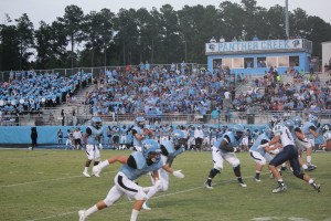 Brendan Magnum, Panther Creek quarterback, takes the snap while Daniel Gleiberman, Leesville defensive end, rushes around the end, and the packed home crowd watches on.